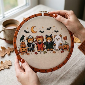 Può includere: Un telaio da ricamo circolare in legno contenente un motivo a punto croce di quattro orsacchiotti vestiti con costumi di Halloween, tra cui uno scheletro, un diavolo, un pipistrello e un fantasma, circondati da zucche e una luna crescente.