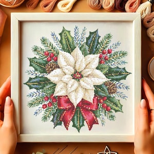 Puede incluir: Obra de arte de punto de cruz enmarcada con un diseño de flor de pascua. La flor de pascua blanca está rodeada de hojas verdes, bayas rojas y un lazo rojo. La obra de arte incluye piñas y ramas de hoja perenne, creando un tema festivo.
