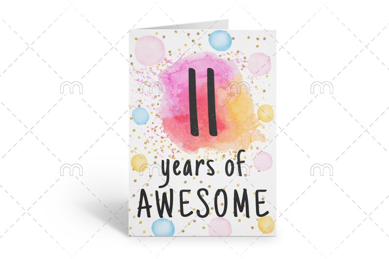 May include: A white card with a watercolor background in shades of pink, orange, and yellow. The number "11" is written in black on the watercolor background. The text "years of AWESOME" is written in black below the number. The card is decorated with gold glitter and small colorful dots.