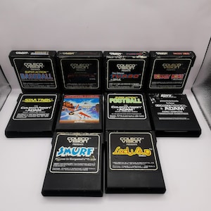 May include: A collection of ten ColecoVision video game cartridges. Titles include "Baseball", "Turbo", "Donkey Kong", "Star Trek", "Smurf", and "Lady Bug". The cartridges are black with colorful game labels.