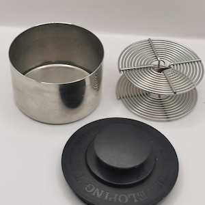 Może przedstawiać: Biały ceramiczny kubek z czarnym uchwytem i napisem "But First, Coffee" czarną, pogrubioną czcionką. Kubek stoi na drewnianej powierzchni. Kubek ma około 10 cm wysokości.