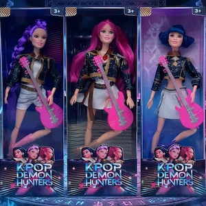 May include: Three KPOP Demon Hunters dolls in clear packaging. Each doll has a different hair colour: purple, pink, and blue. They wear black jackets, white skirts, and hold pink electric guitars. The packaging features the text "KPOP DEMON HUNTERS".