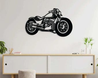May include: Black metal motorcycle wall art. The motorcycle silhouette features a detailed design of the engine, wheels, and handlebars. The artwork is mounted on a white wall above a white cabinet with wooden legs.