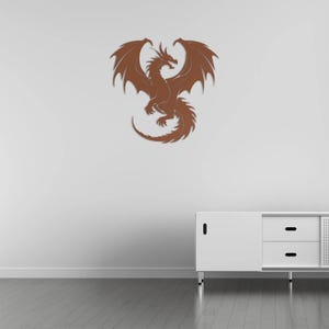 Pu&ograve; includere: Un'opera d'arte da parete a forma di drago in metallo marrone con ali spiegate e coda arricciata. Il drago &egrave; montato su una parete bianca sopra un mobile bianco con due cassetti. Il design del drago &egrave; dettagliato.