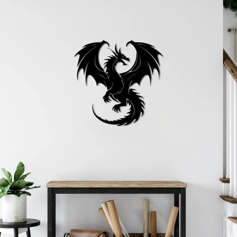 Pu&ograve; includere: Un'opera d'arte da parete a forma di drago in metallo nero con le ali spiegate. Il drago &egrave; una silhouette, con dettagli intricati nelle ali, nel corpo e nella coda. L'opera &egrave; montata su una parete bianca.