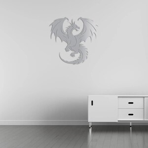 Pu&ograve; includere: Decorazione murale a forma di drago color argento con ali spiegate, coda arricciata e squame dettagliate. Il drago &egrave; montato su una parete bianca sopra un mobile bianco con cassetti.