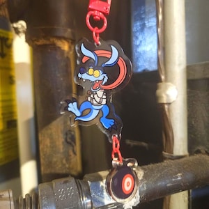 May include: A red keychain with a cartoon monster design. The monster is blue, black, and red with a long tongue. The keychain also has a small, round charm with a vinyl record design.