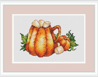 May include: Cross-stitch artwork of a pumpkin-shaped mug filled with white objects, next to a smaller pumpkin. The mug and pumpkin are orange with green leaves. The artwork is framed in a white frame with a pink mat.