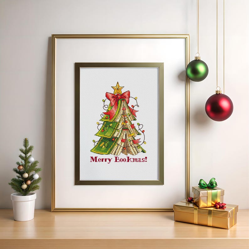 May include: Cross-stitch art of a Christmas tree made of books, adorned with a red bow and star. The phrase "Merry Bookmas!" is stitched below. The framed artwork is displayed with a small tree and ornaments.