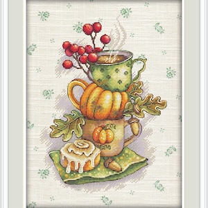 Peut inclure: Une broderie représentant une pile de tasses sur le thème de l'automne et un roulé à la cannelle. La tasse du haut est verte à pois blancs, avec de la vapeur qui s'en échappe. Une tasse en forme de citrouille est en dessous.