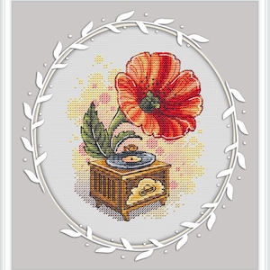 May include: Cross-stitch design featuring a red and orange poppy flower with a green leaf, positioned above a vintage wooden gramophone. The design is set within a white oval frame with leaf accents, on a gray background.