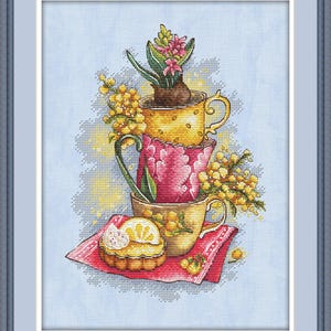 Peut inclure: Broderie au point de croix représentant trois tasses empilées, chacune avec un motif floral différent. La tasse supérieure contient une plante en pot avec des fleurs roses. Une petite tarte au citron repose sur une serviette rouge.