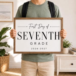 Puede incluir: Un letrero rectangular con marco de madera, fondo blanco y texto negro que dice First Day of SEVENTH GRADE 2026-2027. El letrero presenta una combinación de fuentes cursivas y serif, con líneas horizontales flanqueando el texto superior.