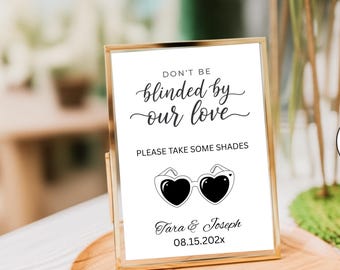 May include: A framed sign with the text "DON'T BE blinded by our love" and "PLEASE TAKE SOME SHADES". Below is a graphic of heart-shaped sunglasses. The sign is in a gold frame and includes the names Tara & Joseph and a date.