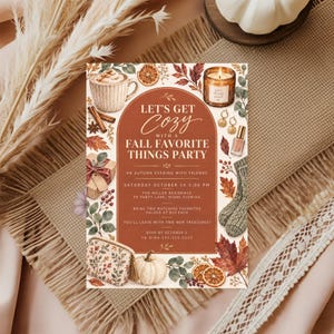 May include: A rectangular party invitation card with a rust-colored arched center featuring the text LET'S GET COZY WITH A FALL FAVORITE THINGS PARTY. The border is decorated with illustrations of a mug, cinnamon sticks, candle, gift, socks, and pumpkin.