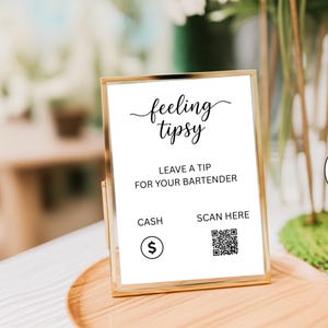 May include: A gold-framed sign with the words "feeling tipsy" in cursive script. The sign reads "Leave a tip for your bartender" and includes a cash symbol and a QR code for scanning.