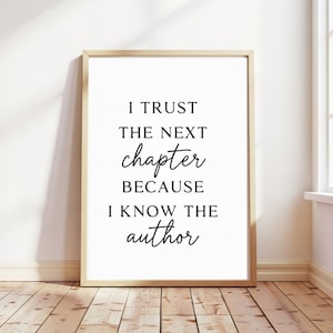 May include: A framed print with the quote "I trust the next chapter because I know the author" in black script. The frame is a light wood color, and the background is white. The print is displayed on a wooden floor.