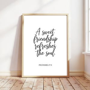Puede incluir: Un estampado enmarcado con la cita "A sweet friendship refreshes the soul" en escritura negra. El estampado está en un marco de madera clara e incluye el texto "PROVERBIOS 27:9". El fondo es blanco.