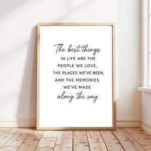 Op de afbeelding: Een ingelijste print met de tekst "The best things in life are the people we love, the places we've been, and the memories we've made along the way." De lijst is lichtbruin en de tekst is zwart.