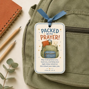 May include: A rectangular tag with a blue ribbon featuring the text PACKED WITH PRAYER! and an illustration of a backpack with books and a cross. Below is the text: May God protect you, lead you, and help your light shine wherever this school year takes you. PSALM 121:8.