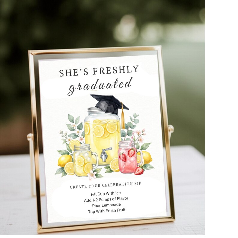 May include: A gold-framed sign featuring the text SHE'S FRESHLY graduated and CREATE YOUR CELEBRATION SIP with instructions. The illustration shows a large lemonade dispenser and two mason jars with lemons, strawberries, and a graduation cap.