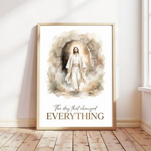 May include: A framed print with a watercolour illustration of a figure in white robes emerging from a stone structure. The text "The day that changed EVERYTHING" is below the image. The artwork has a soft, ethereal quality.