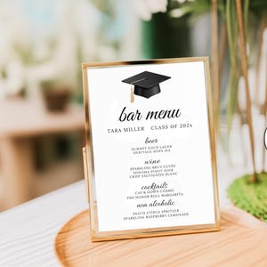 Puede incluir: Un menú de bar enmarcado en dorado con un gráfico de birrete. El menú enumera cerveza, vino, cócteles y bebidas sin alcohol. El texto incluye "TARA MILLER CLASS OF 202x" y opciones como "Peach Citrus Spritzer".