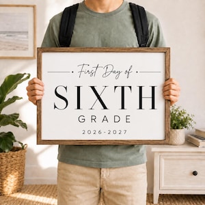 May include: A rectangular wooden framed sign with a white background and black text that reads First Day of SIXTH GRADE 2026-2027. The sign features a clean, bold font for the grade level and a script font for the opening phrase.