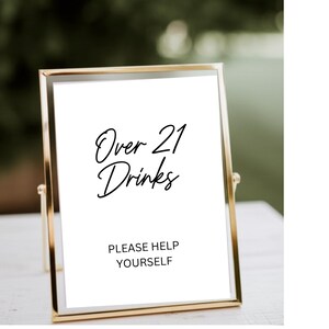 Op de afbeelding: Een goudkleurig omlijst bord met de tekst "Over 21 Drinks" in elegant schrift. Daaronder staat "PLEASE HELP YOURSELF". Het bord staat tegen een vage groene achtergrond, wat duidt op een buitenevenement of bijeenkomst.