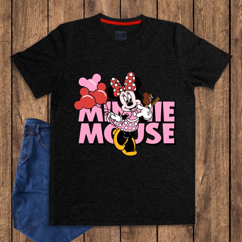 May include: Black t-shirt featuring Minnie Mouse holding balloons and a chocolate treat. The text "MINNIE MOUSE" is in pink. The shirt has a red collar and is paired with blue jeans.
