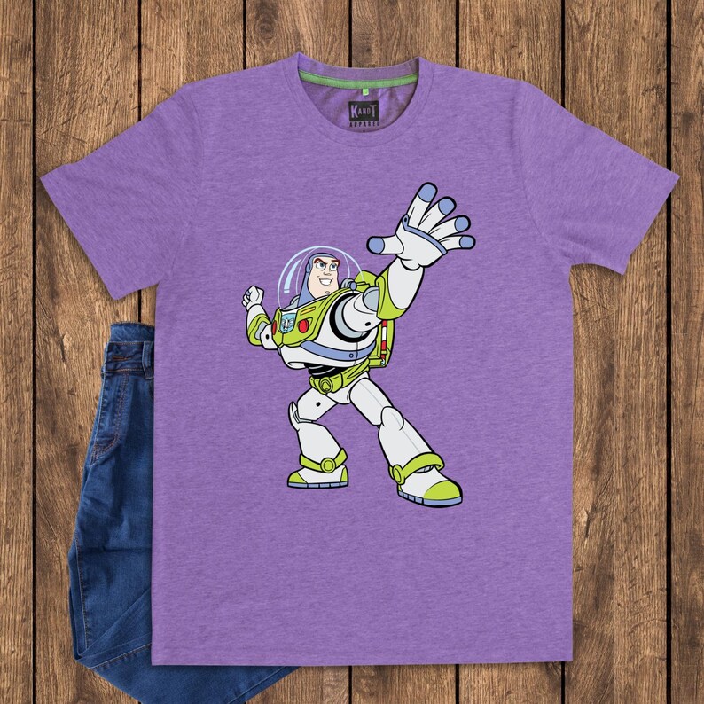 May include: A purple t-shirt featuring a cartoon illustration of Buzz Lightyear from Toy Story. The character is depicted in his signature space ranger suit, with white, green, and blue accents. The shirt is paired with blue denim shorts.