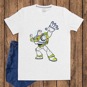 May include: A light gray t-shirt featuring a cartoon illustration of Buzz Lightyear from Toy Story. The character is depicted in his signature white, green, and purple spacesuit, with his arm raised. A pair of blue jeans is visible.
