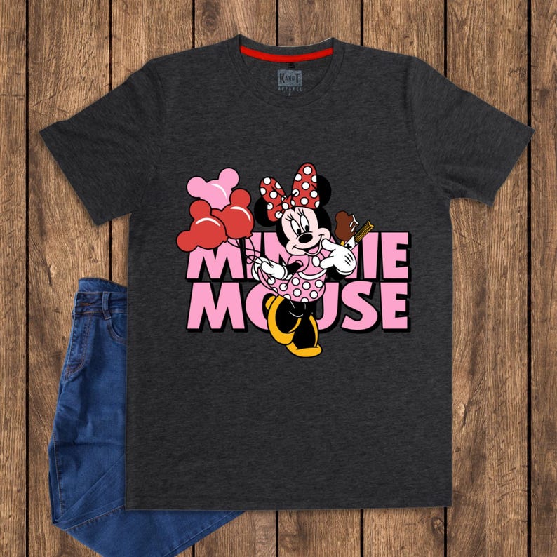 May include: Dark gray t-shirt featuring a graphic of Minnie Mouse holding balloons and a popsicle. The text "MINNIE MOUSE" is printed in pink. A pair of blue jeans is visible on the left side of the image.