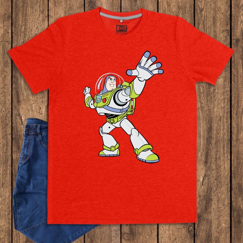 May include: A red t-shirt featuring a cartoon illustration of Buzz Lightyear from Toy Story. The character is depicted in his signature space ranger suit, with a white and green color scheme. The shirt is paired with blue jeans.