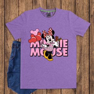 May include: A purple t-shirt featuring a graphic of Minnie Mouse holding balloons and a chocolate treat. The text "MINNIE MOUSE" is printed in pink and black. A pair of blue jeans is visible on the left side.