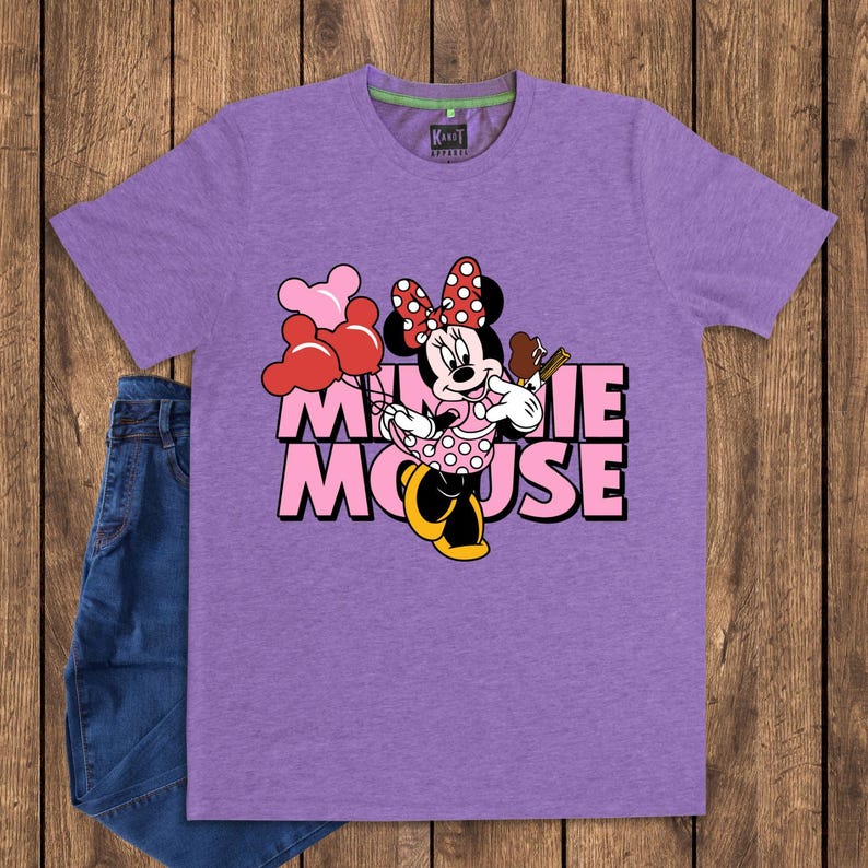 May include: A purple t-shirt featuring a graphic of Minnie Mouse holding balloons and a chocolate treat. The text "MINNIE MOUSE" is printed in pink and black. A pair of blue jeans is visible on the left side.