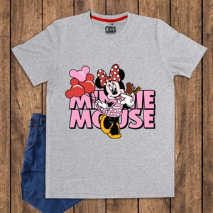 May include: A gray t-shirt featuring a Minnie Mouse graphic. The design includes Minnie Mouse holding balloons and a treat, with the words "Minnie Mouse" in pink. The shirt has a red collar and a brand label.