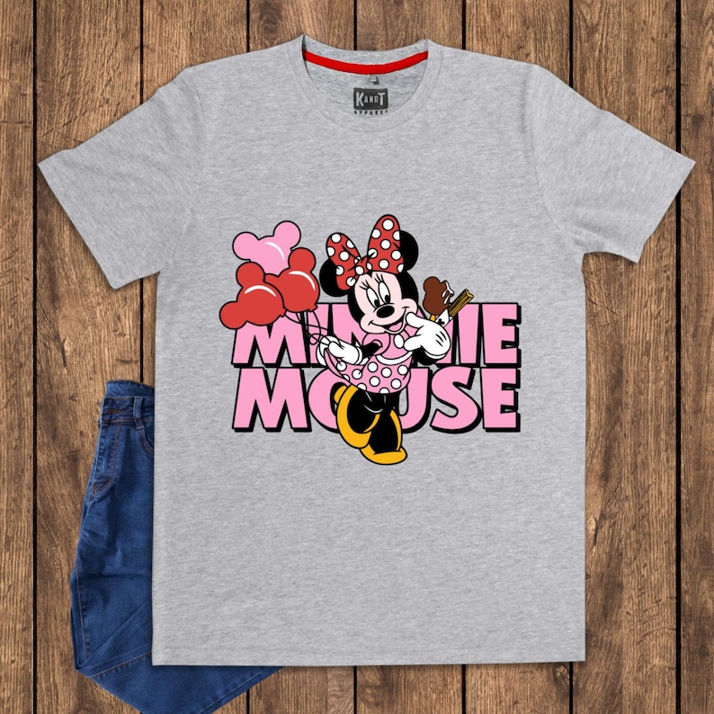 May include: A gray t-shirt featuring a Minnie Mouse graphic. The design includes Minnie Mouse holding balloons and a treat, with the words "Minnie Mouse" in pink. The shirt has a red collar and a brand label.