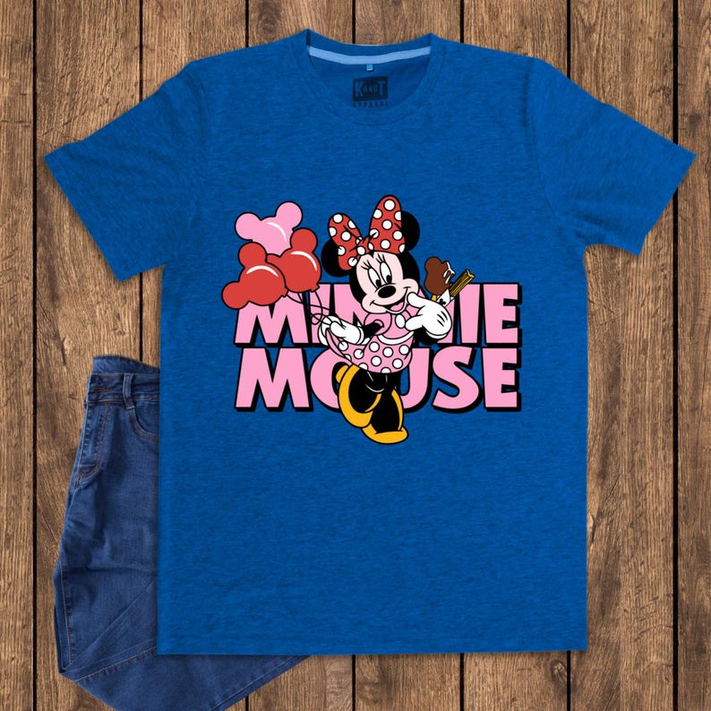 May include: A blue t-shirt featuring a graphic of Minnie Mouse holding balloons and a chocolate bar. The text "MINNIE MOUSE" is printed in pink. A pair of blue jeans is visible on the left side of the image.