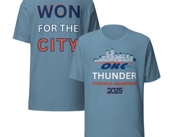 Może przedstawiać: Jasnoniebieska koszulka z napisem "WON FOR THE CITY" na plecach w kolorze białym i pomarańczowym. Przód koszulki zdobi napis "OKC THUNDER NATIONAL CHAMPIONS 2025" z grafiką panoramy miasta.