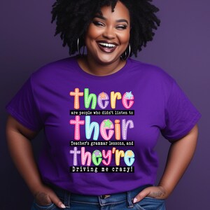 Puede incluir: Una camiseta morada con las palabras "there", "their" y "they're" en fuentes coloridas y divertidas. El texto hace referencia con humor a las lecciones de gramática y a la frustración por los errores gramaticales. El diseño de la camiseta es llamativo y divertido.