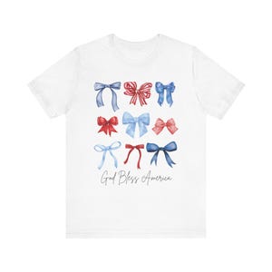 May include: White t-shirt with a red, white, and blue bow design and the text "God Bless America".