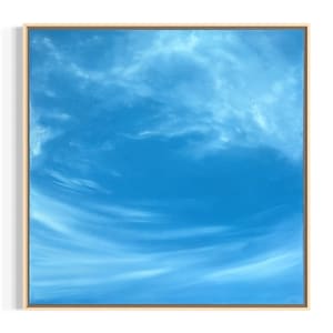 Könnte beinhalten: Quadratische Leinwandkunst mit einem leuchtend blauen Himmel mit zarten weißen Wolken. Das Kunstwerk ist in einem hellfarbigen Holzrahmen gerahmt, was eine ruhige und luftige Ästhetik schafft. Der Farbverlauf des Himmels verleiht Tiefe.