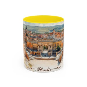 May include: A ceramic coffee mug with a yellow interior and a detailed image of Plovdiv, Bulgaria. The exterior features a cityscape with buildings, arches, and a scenic landscape. The word "Plovdiv" is printed in a script font.