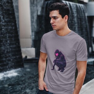 Puede incluir: Una camiseta gris con un gráfico de una persona con una sudadera con capucha con un brillo rosa alrededor de la cara.