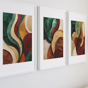 Puede incluir: Tres impresiones artísticas abstractas enmarcadas. Cada impresión presenta formas fluidas en tonos verdes, rojos, beige y marrones. La obra de arte está encerrada en un marco blanco, creando una estética moderna. El arte se exhibe en una pared blanca.