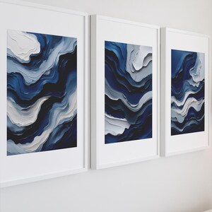 Puede incluir: Tres impresiones artísticas abstractas enmarcadas. Cada impresión presenta un diseño texturizado con tonos de azul marino, blanco y gris, creando un efecto en capas similar a las olas. Las impresiones se exhiben en marcos blancos, agregando una estética limpia y moderna a la decoración de la pared.