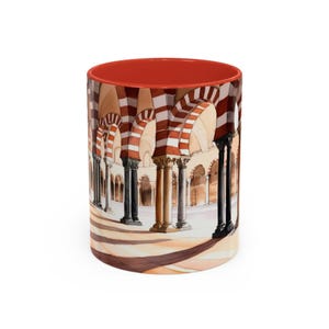 Peut inclure: Une tasse en céramique avec un intérieur rouge, ornée d'une illustration à l'aquarelle d'une colonnade arquée. Le motif présente des rayures rouges et blanches alternées sur les arches et les colonnes, créant un motif architectural saisissant.
