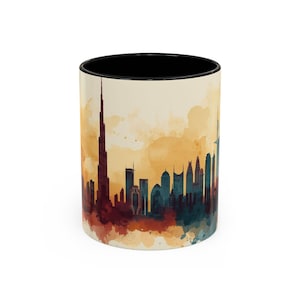 May include: A white ceramic coffee mug with a black interior. The mug features a watercolor-style illustration of the Dubai skyline in shades of red, teal, and brown against a cream-colored background.
