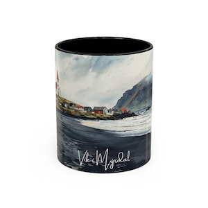 Könnte beinhalten: Weißer Keramikbecher mit schwarzem Innenraum, mit einem Aquarellgemälde eines Küstendorfes mit Kirche und rotbedachten Häusern. Der Becher trägt den Schriftzug "Vik i Myrdal" in einer Schreibschrift.
